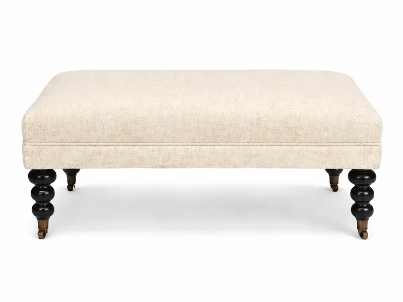 Cream-colored upholstered bench with black and wooden turned legs.