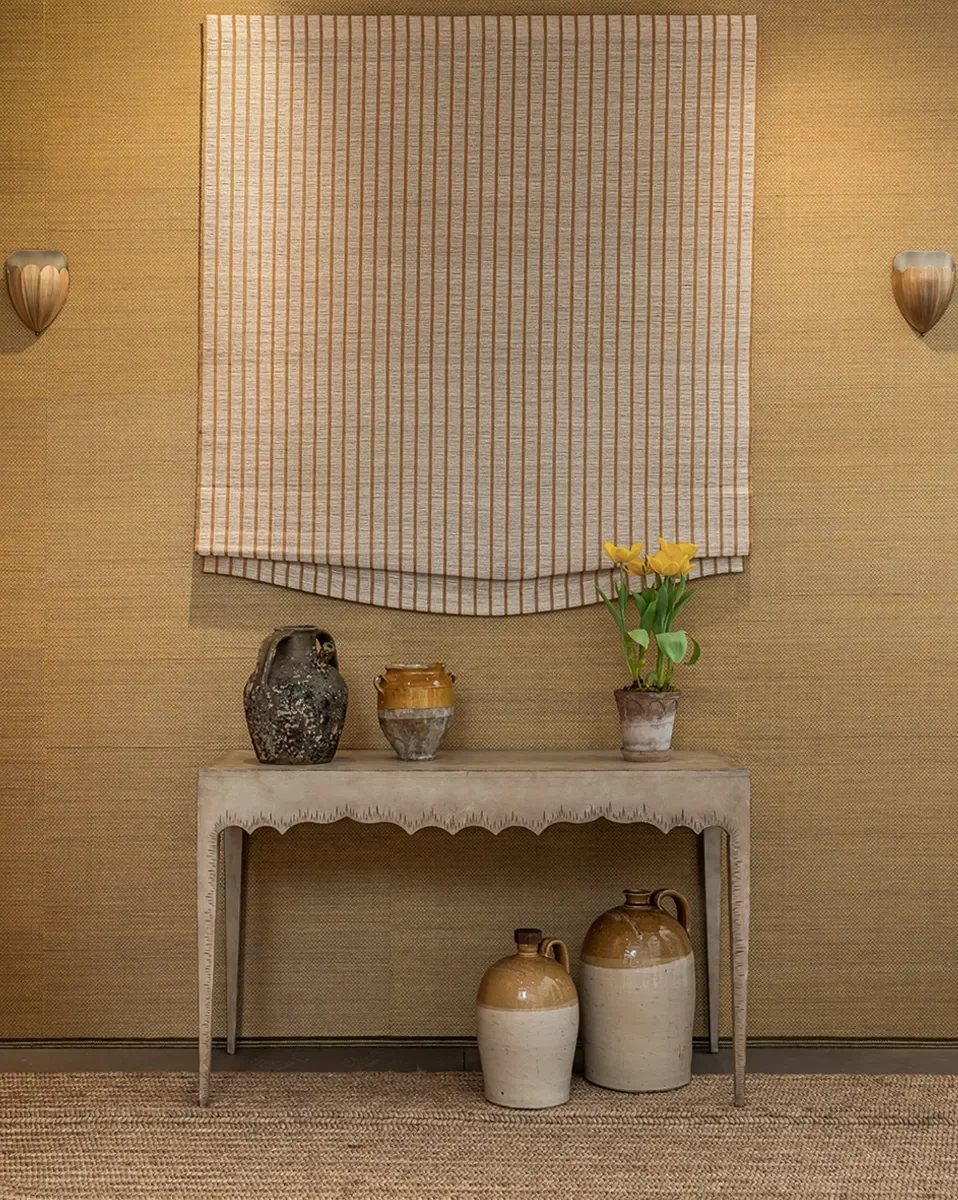 A beige textured wall with a striped cloth hanging, a beige table with decorative pottery, and a small potted plant with yellow flowers.