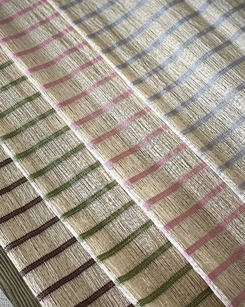 Close-up of woven fabric with horizontal stripes in pink, blue, green, and brown across a beige background.
