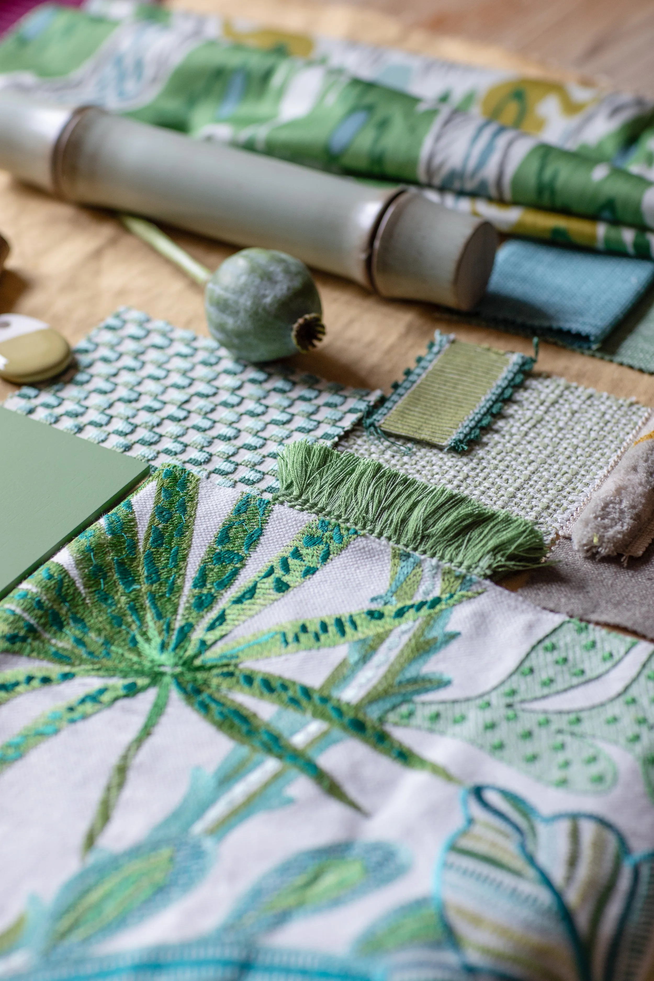 Close-up of green embroidered fabric with a floral pattern, a small round green fruit, and fabric swatches on a wooden surface.