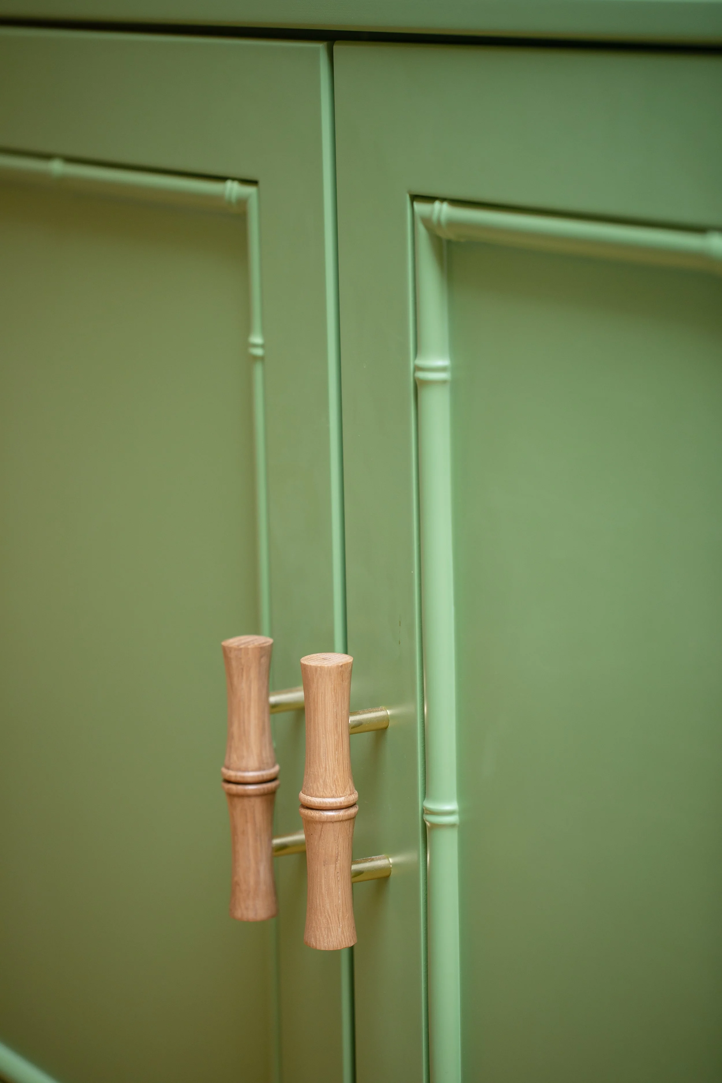 Close-up of a green cabinet with light wood and gold-colored towel bars attached to the doors.