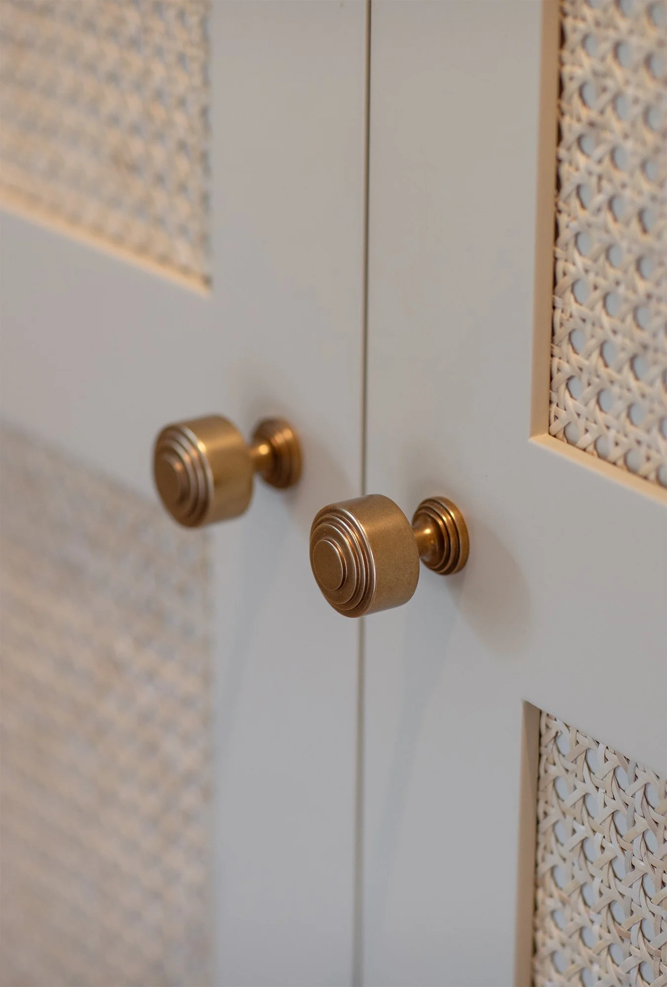 Close-up of a white cabinet with woven cane panels and round brass knobs.