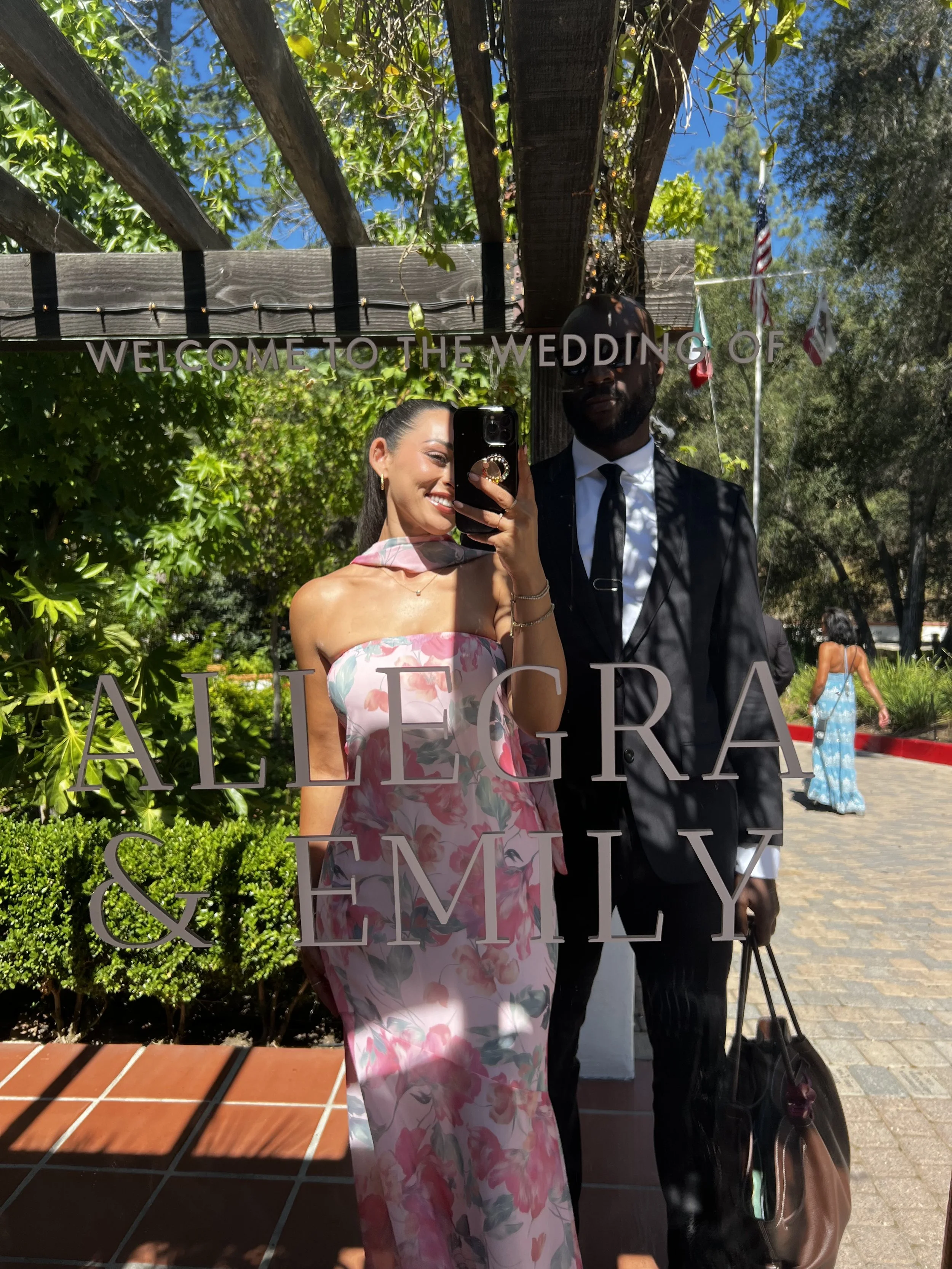 Couple taking a wedding selfie in front of a mirror sign reading “Welcome to the wedding of Semy and Alejandra.”