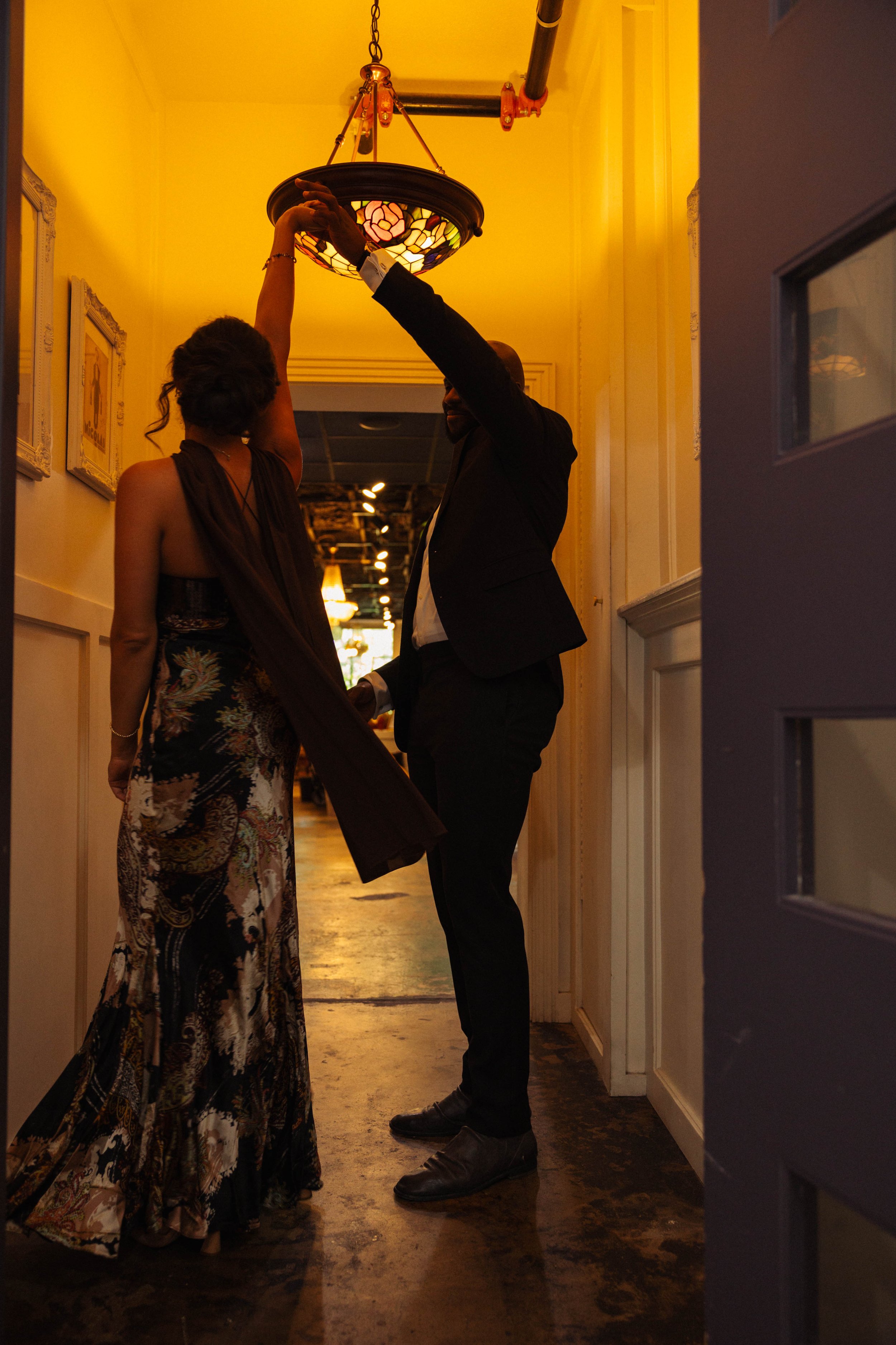 Two people adjust a stained-glass Tiffany-style pendant light in a warmly lit interior.