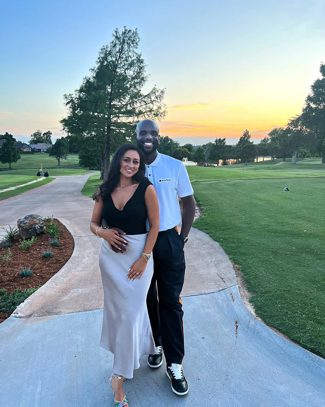 Smiling couple posing on a golf course path at sunset