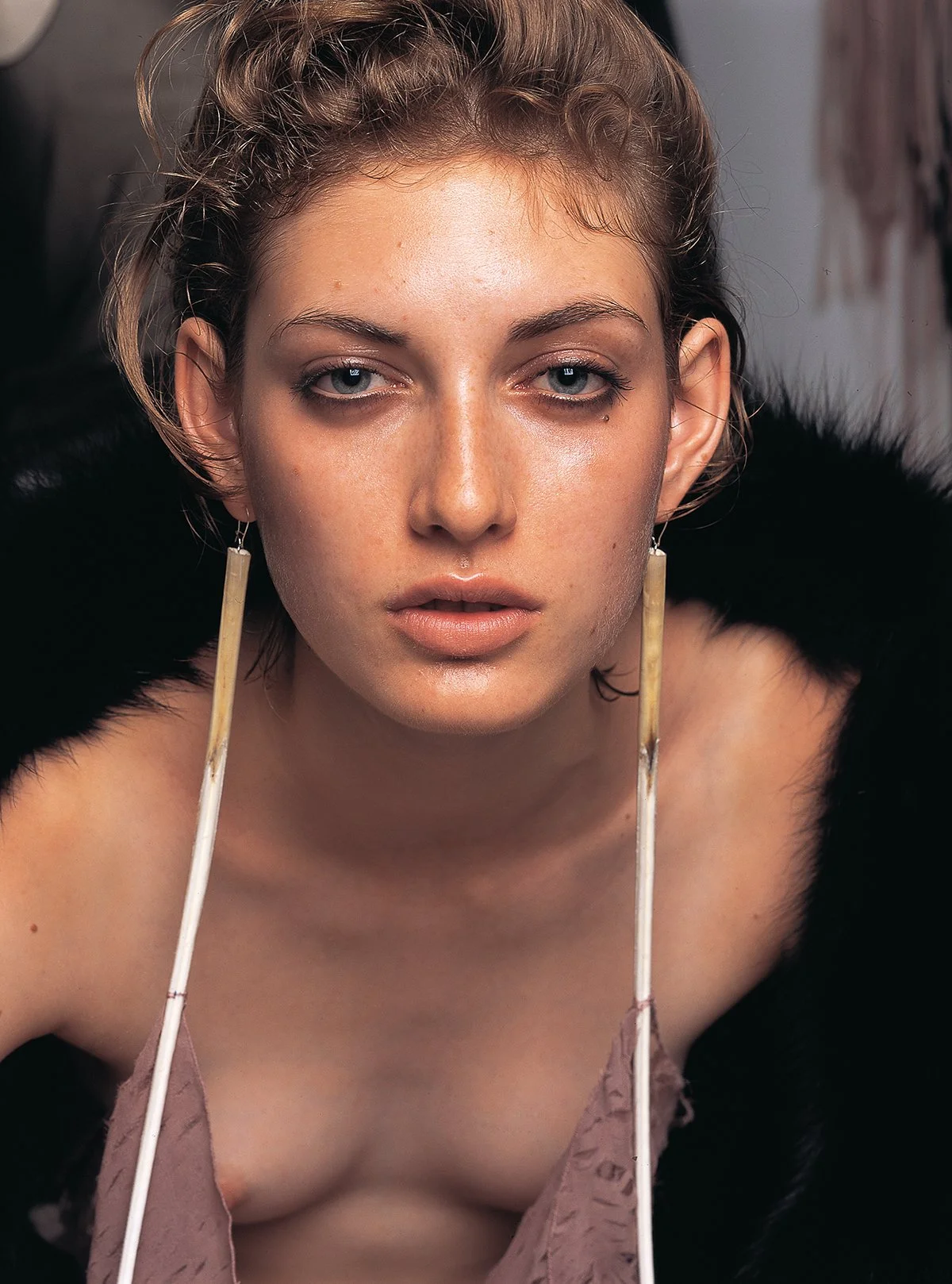 Editorial shot in Paris, of a person with light brown hair in a black coat and long earrings, looking directly at the camera.