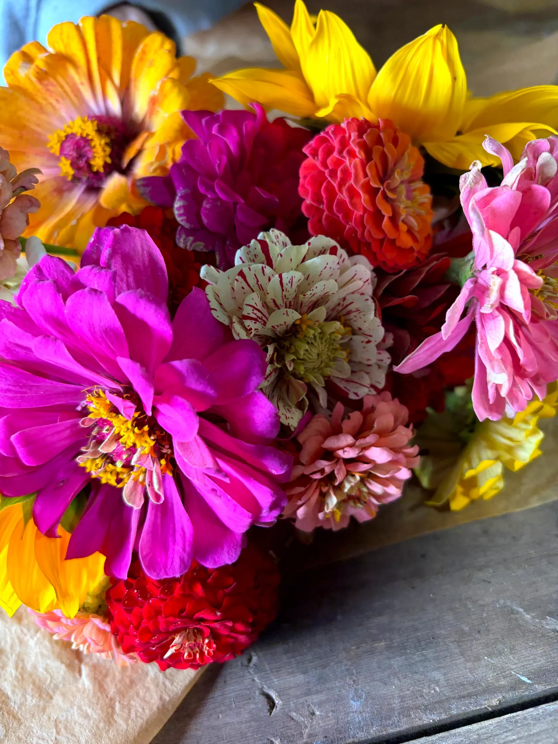 A colorful bouquet of freshly picked flowers including sunflowers, pink, yellow, orange, purple, and white zinnia blossoms.
