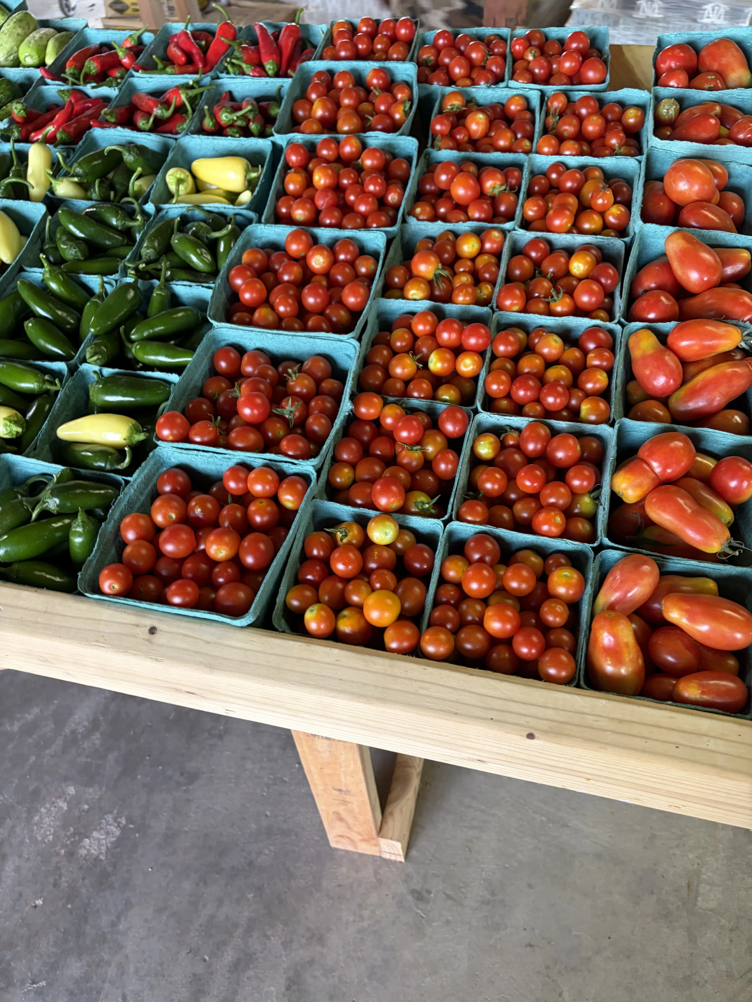 Display of various fresh tomatoes and peppers in grab and go containers for easy shopping.