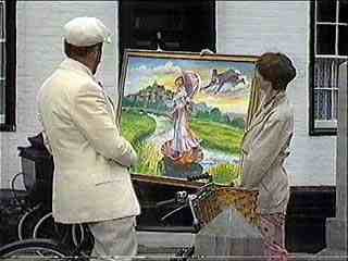 Two men in white suits looking at a colorful landscape painting mounted on an easel outside a building.