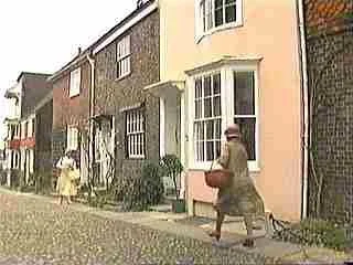People walking along a sidewalk in front of colorful row houses, one person carrying a basket.