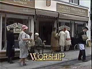 A group of people standing outside a store called 'Short Brothers' with a sign for a 'Grand Opening Sale.' Some people are entering and exiting the shop, with the word 'WORSHIP' overlaid at the bottom of the image.
