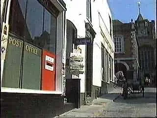 Street scene with a post office, a person walking, and a horse-drawn carriage.