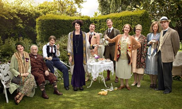 Mapp and Lucia BBC cast standing and sitting around an outdoor table in a garden, enjoying tea or coffee.