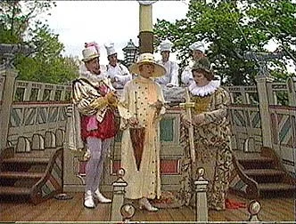 Actors in historical costumes performing on a stage with a backdrop of trees and wooden structures.