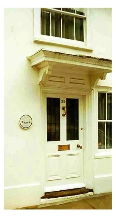 Close-up of a white front door with house number 29, a mailbox, and a brass doorknob, with a window above the door and a window to the right.