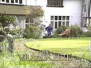 A person in purple clothing watering plants in a garden with a well-maintained lawn and outdoor furniture, with the text 'The Village Fete' at the bottom.