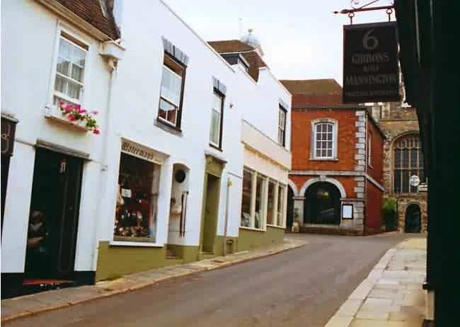 Empty street with white and red brick buildings, some with flower boxes and a sign for a tasting room.