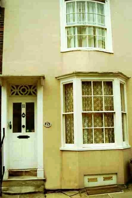 Exterior view of a beige house with large bay window and a white front door with decorative glass and black numbers '11'.