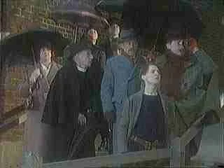 Group of five people standing outdoors, all wearing face masks, with trees and buildings in the background.