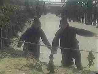 Two people standing outdoors by a fence, holding a fishing rod.