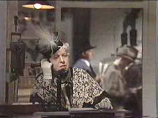 A woman in a leopard print top talking on a vintage telephone, appearing frustrated or upset, in a busy, possibly historical setting.