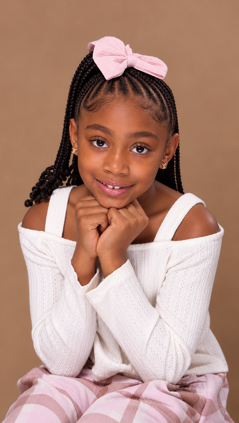 Anaya Floyd, young co-author of Be Nice, posing with her chin resting on her hands, wearing a white off-shoulder top, pink plaid pants, and a pink bow in her braided hair.