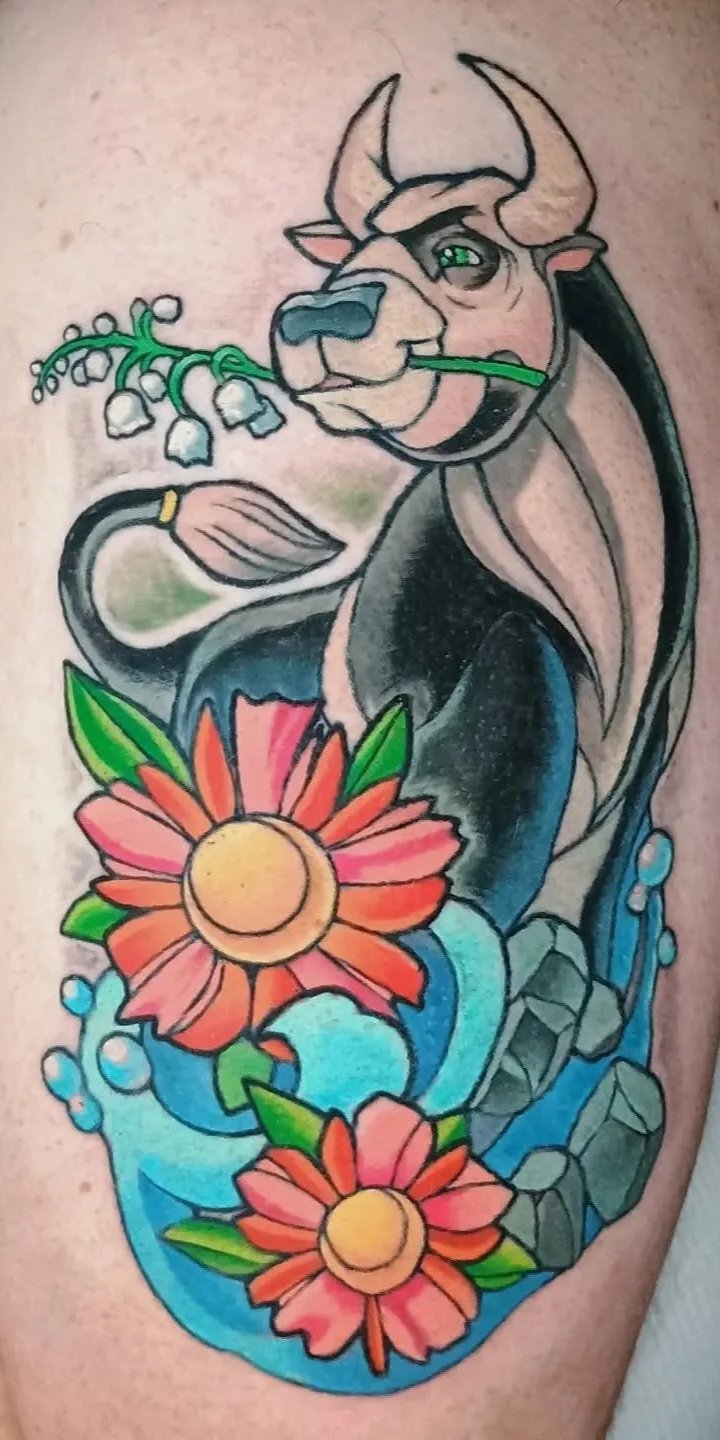Colorful tattoo of a horned winged dragon holding a green stem above pink flowers, blue waves, leaves, and gray stones
