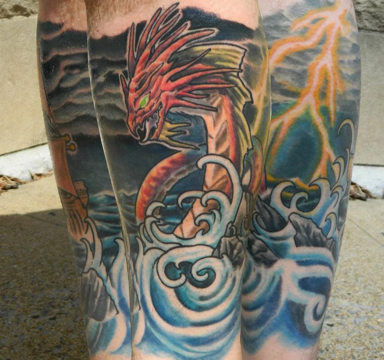 Close-up of an intricate leg tattoo depicting a red dragon surrounded by blue ocean waves, yellow lightning, and dark clouds.