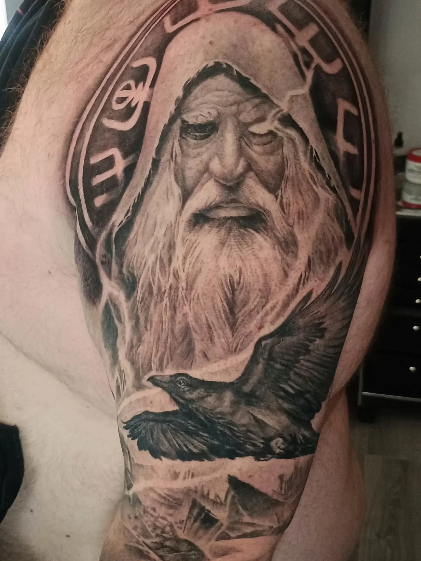 Detailed tattoo of a bearded Viking warrior with ravens and Norse-inspired lettering on an upper arm