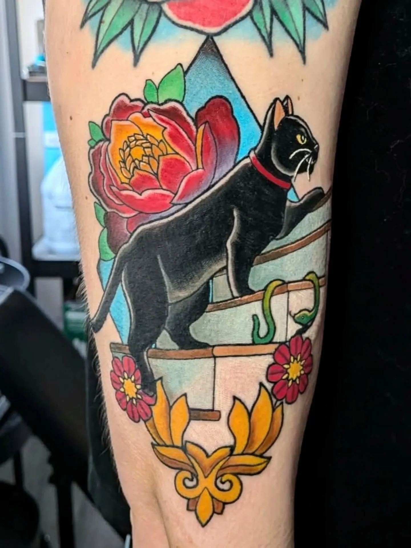 Colorful tattoo featuring a black cat perched on a flower-adorned window box, with roses, a snake, flames, and botanical designs.