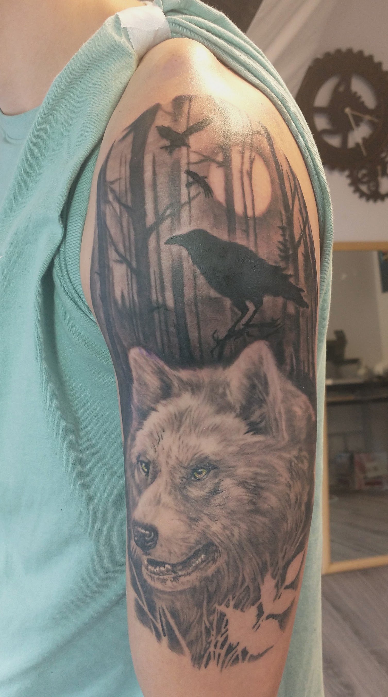 Close-up of a detailed black-and-gray upper-arm tattoo depicting a lion beneath a crow in a forest.