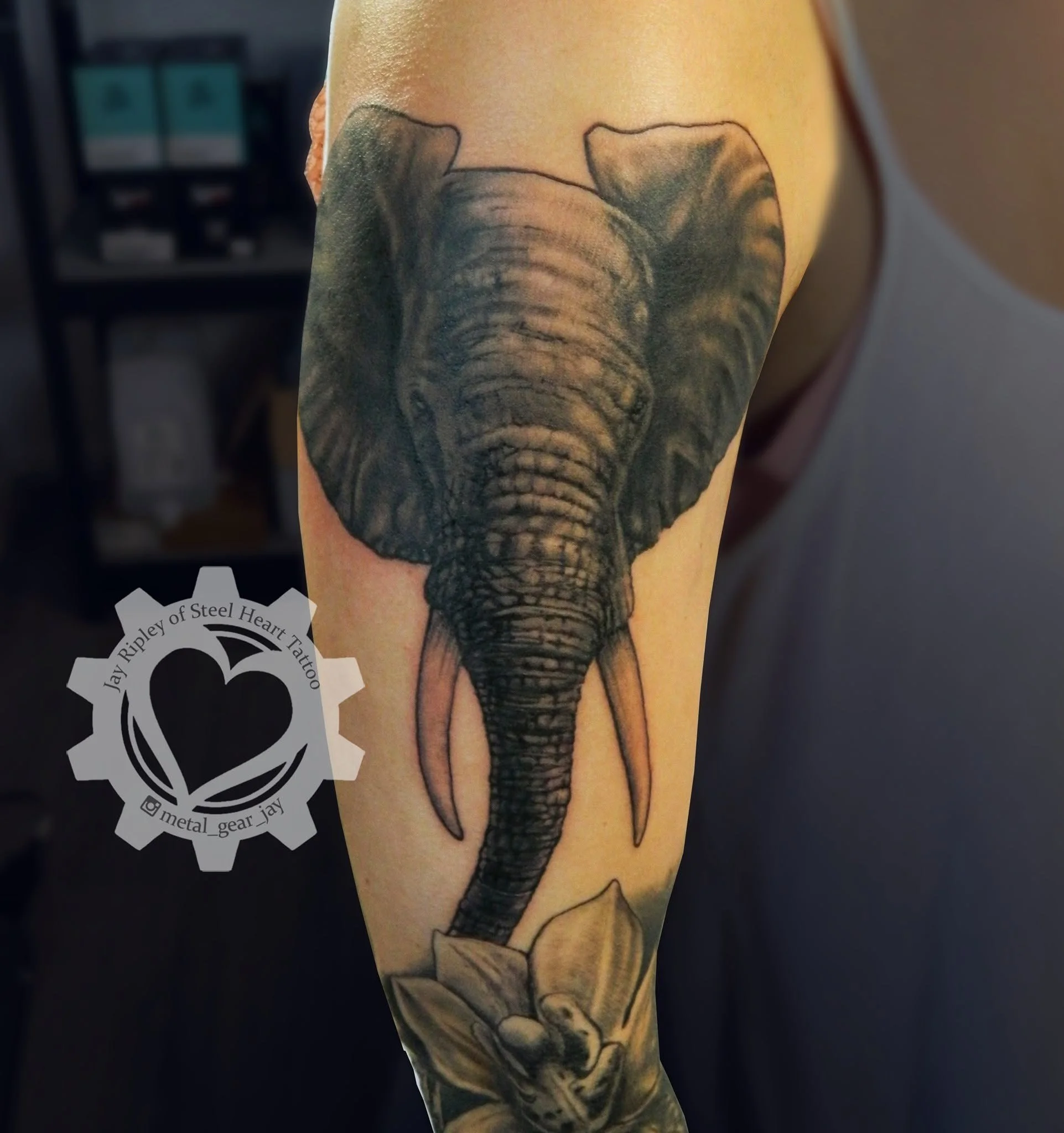 Realistic elephant tattoo on a person’s upper arm, surrounded by floral artwork