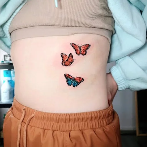 Three colorful butterfly tattoos on a person's lower back