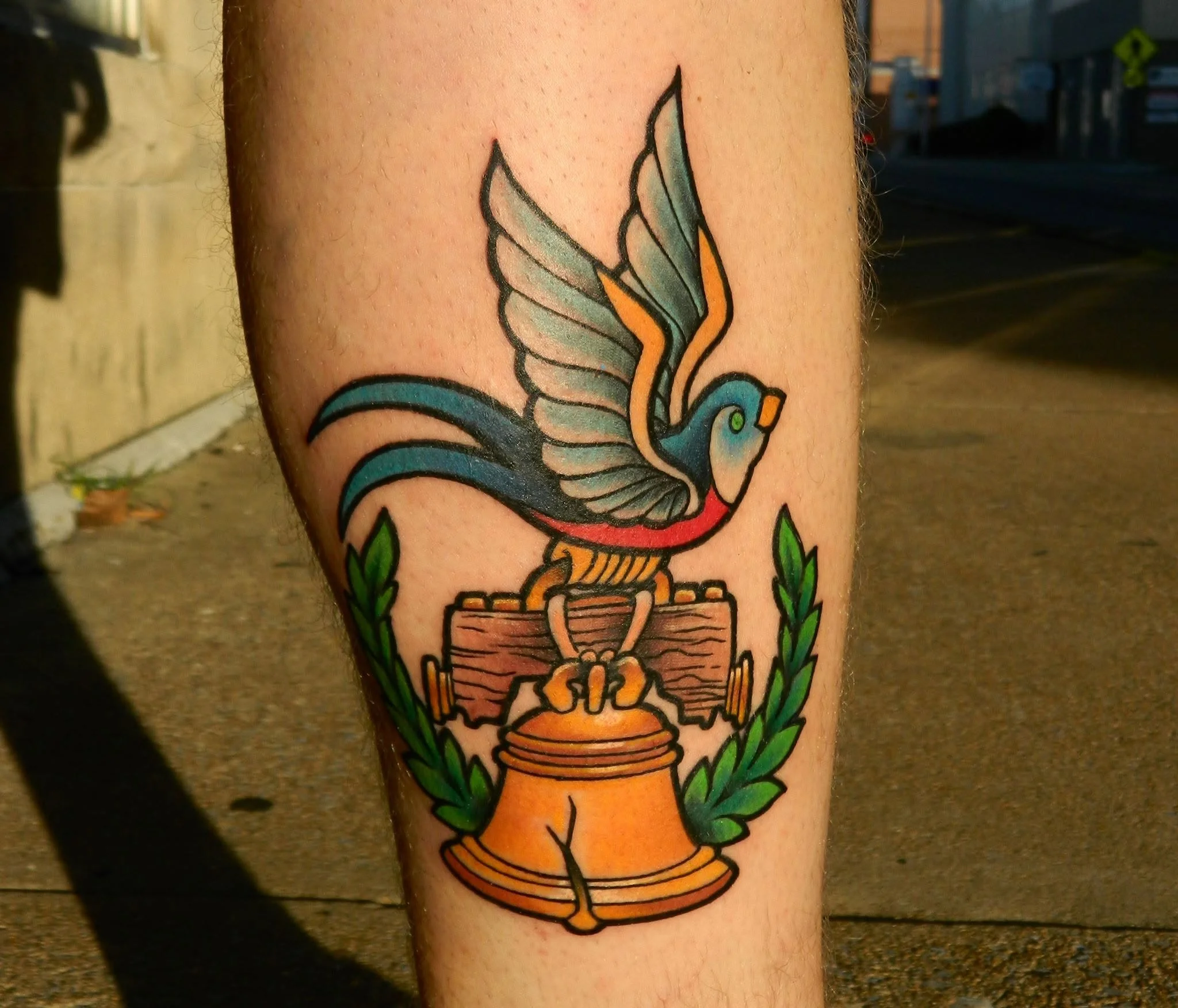 Colorful leg tattoo featuring a blue-winged bird perched on a wooden sign above a honey pot, framed by green leaves.