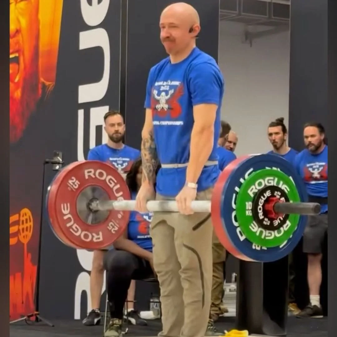 Weightlifter performing a barbell deadlift with Rogue bumper plates on a competition stage