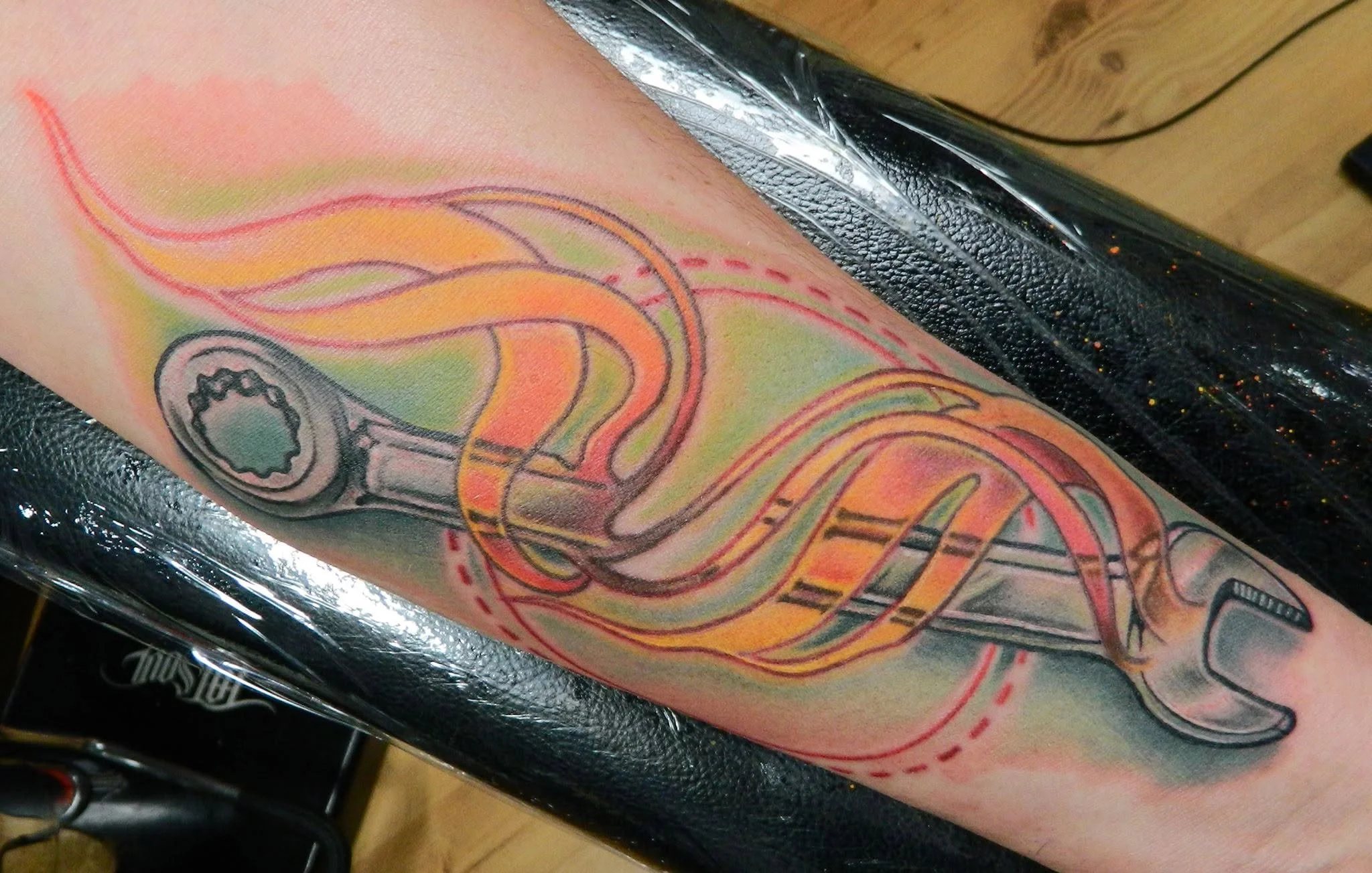 Close-up of a colorful abstract tattoo featuring looping lines and mechanical shapes on a person's forearm.