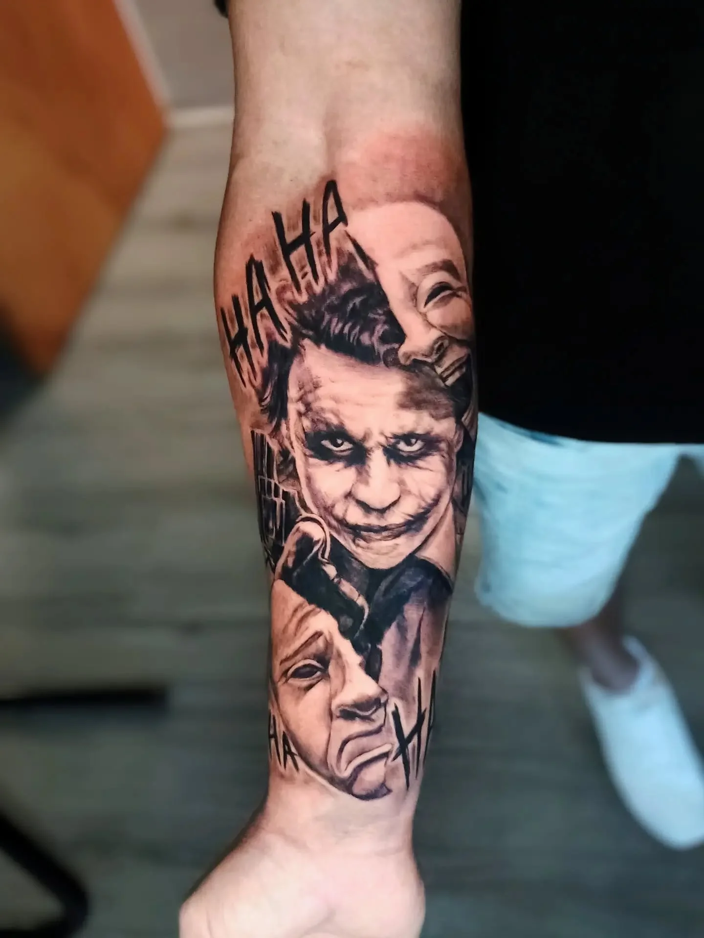 Close-up of a forearm tattoo featuring stylized portraits of the Joker and other comic book characters with bold lettering.