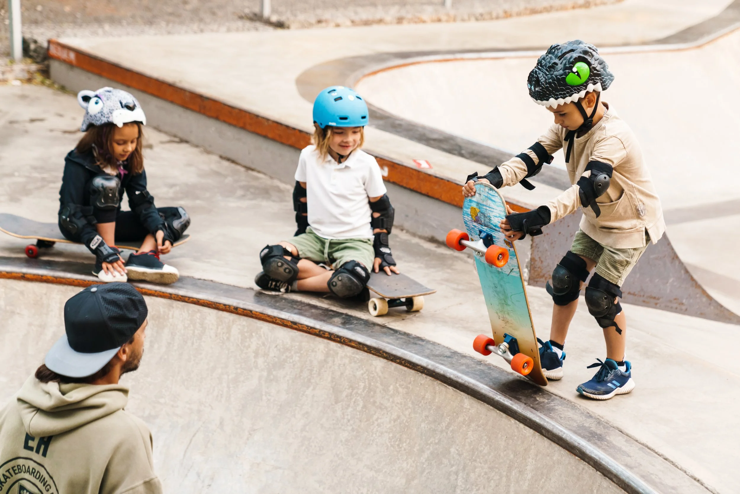 Children wearing helmets and protective pads skateboard together at an outdoor skate park.
