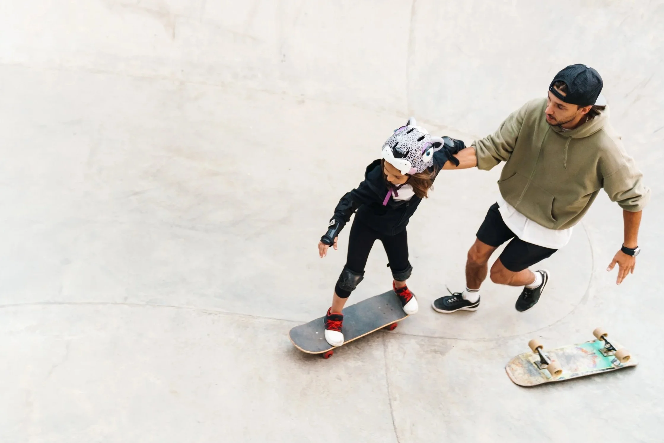 Adult helping a child learn to skateboard at a skate park, skateboarder, skate instructor, having fun outside, fresh air, nuture, play, structure, health.