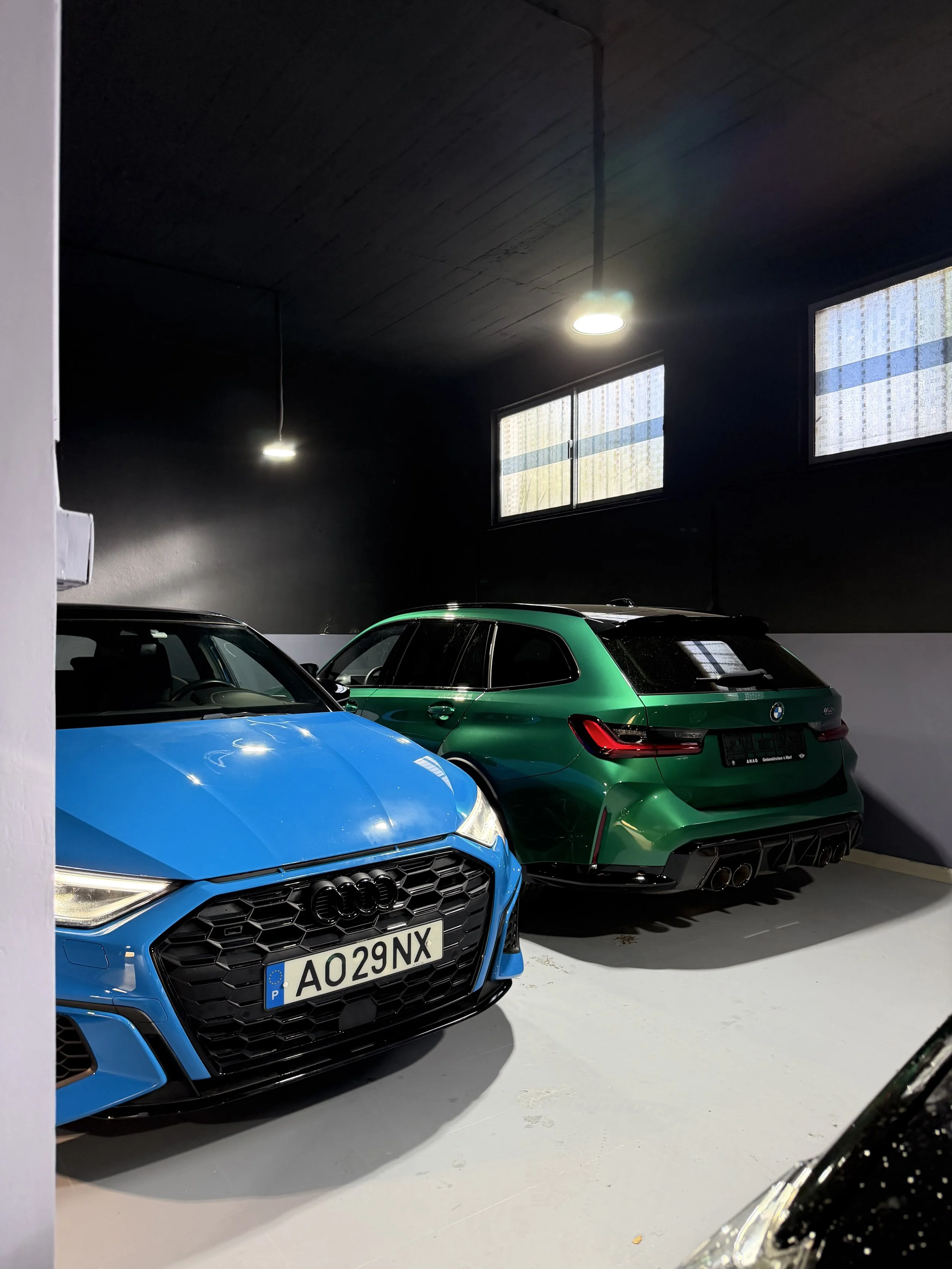 Multiple sports cars parked indoors in the Bainbridge & Co High-End Car Storage, in a nicely lit garage with black walls and barricaded windows.