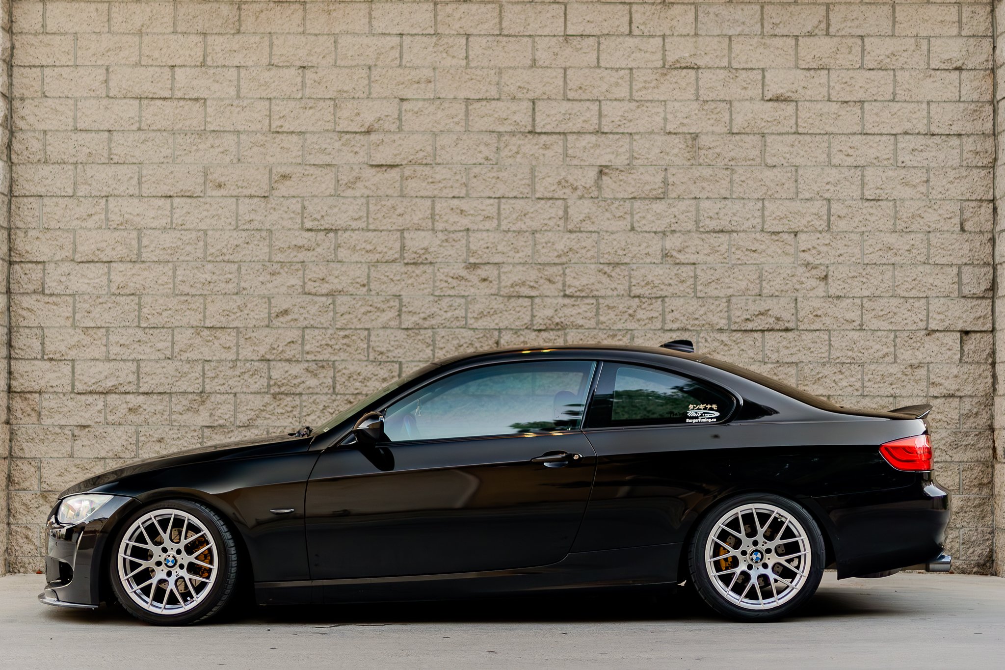 Side view of a black BMW sports car parked in front of a beige brick wall