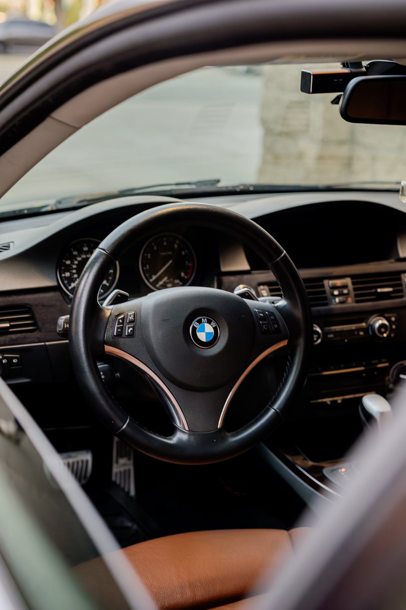 Inside view of a car with a BMW steering wheel and dashboard, viewed through an open sun visor or partial view.