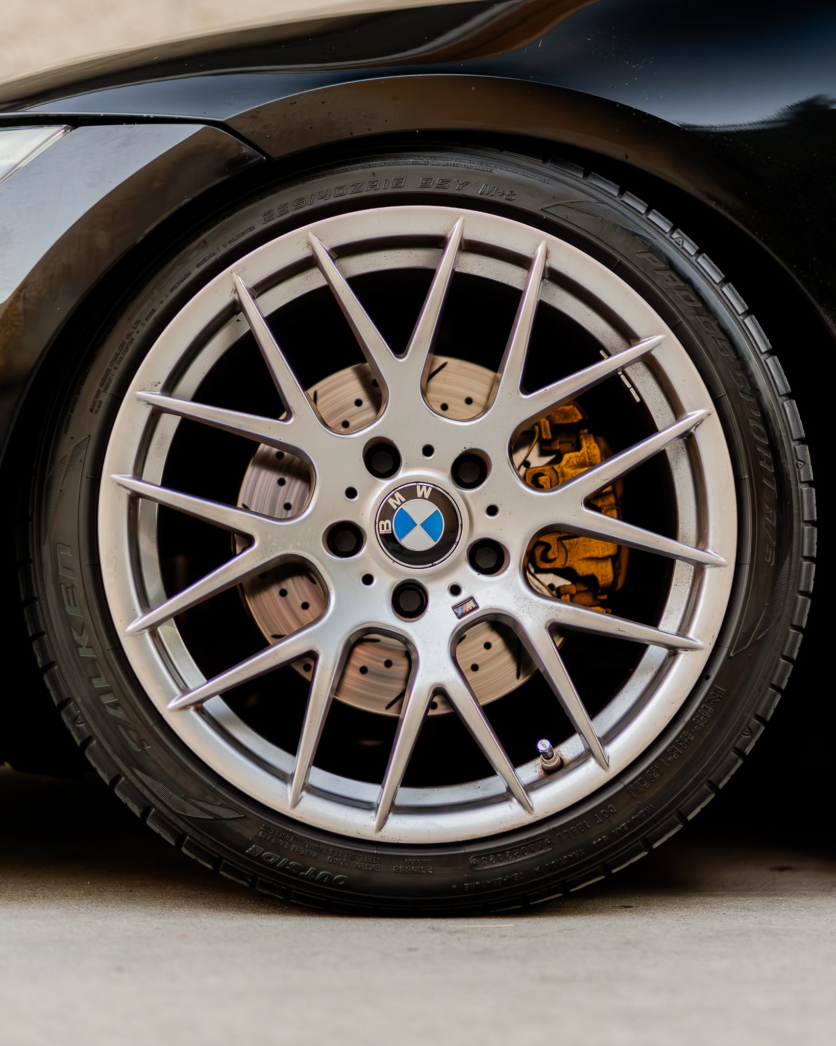 Close-up of a black BMW car wheel with a silver alloy rim, BMW logo in the center, and a tire displaying size and specifications.