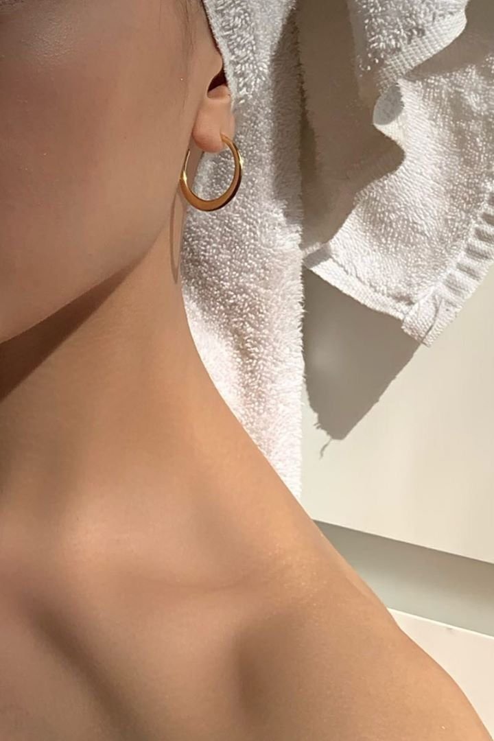 Close-up of a person’s ear and neck wearing a small gold hoop earring beside a white textured towel.