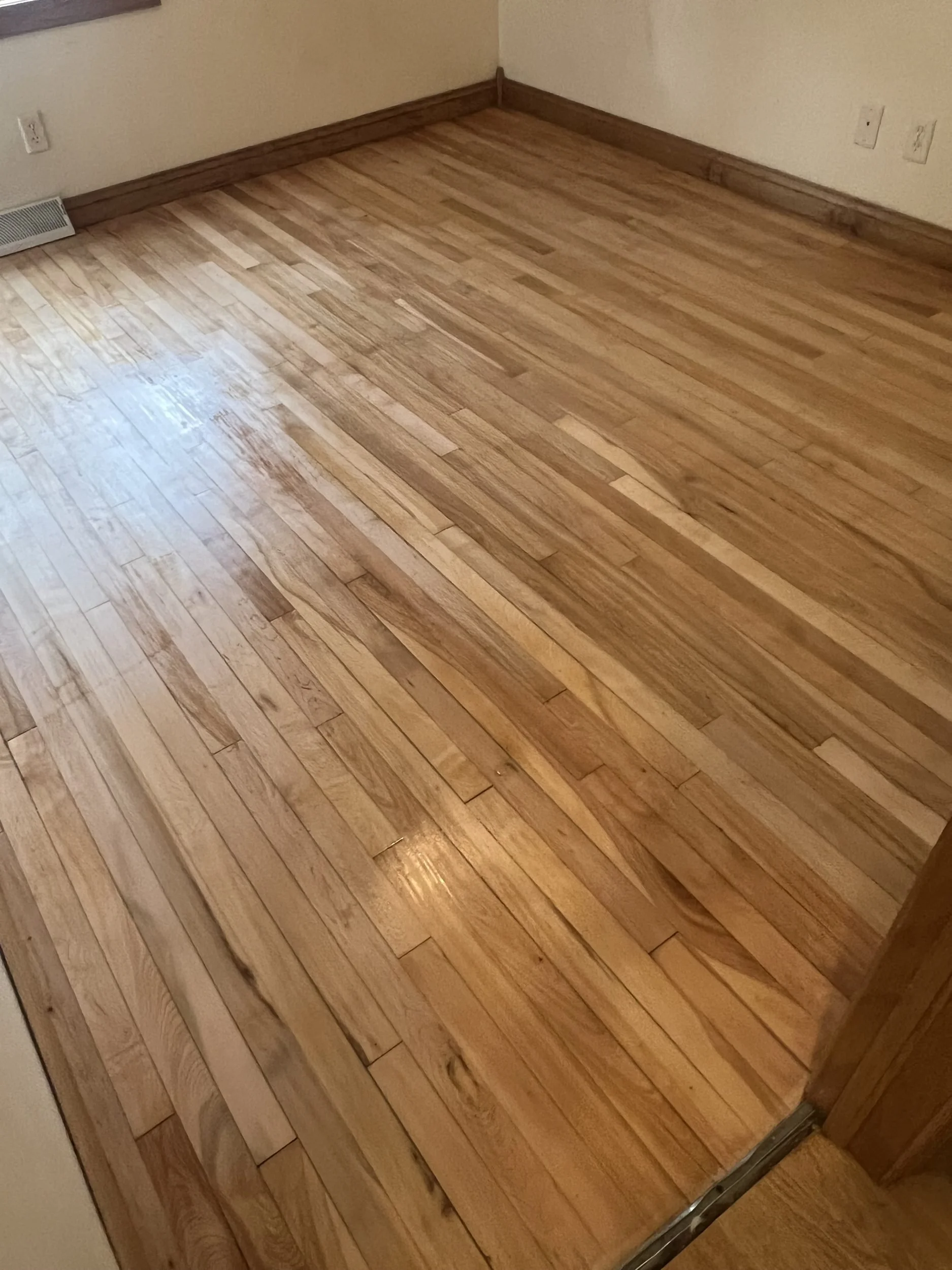 Empty room with hardwood flooring, beige walls, electrical outlets, and baseboard heater.