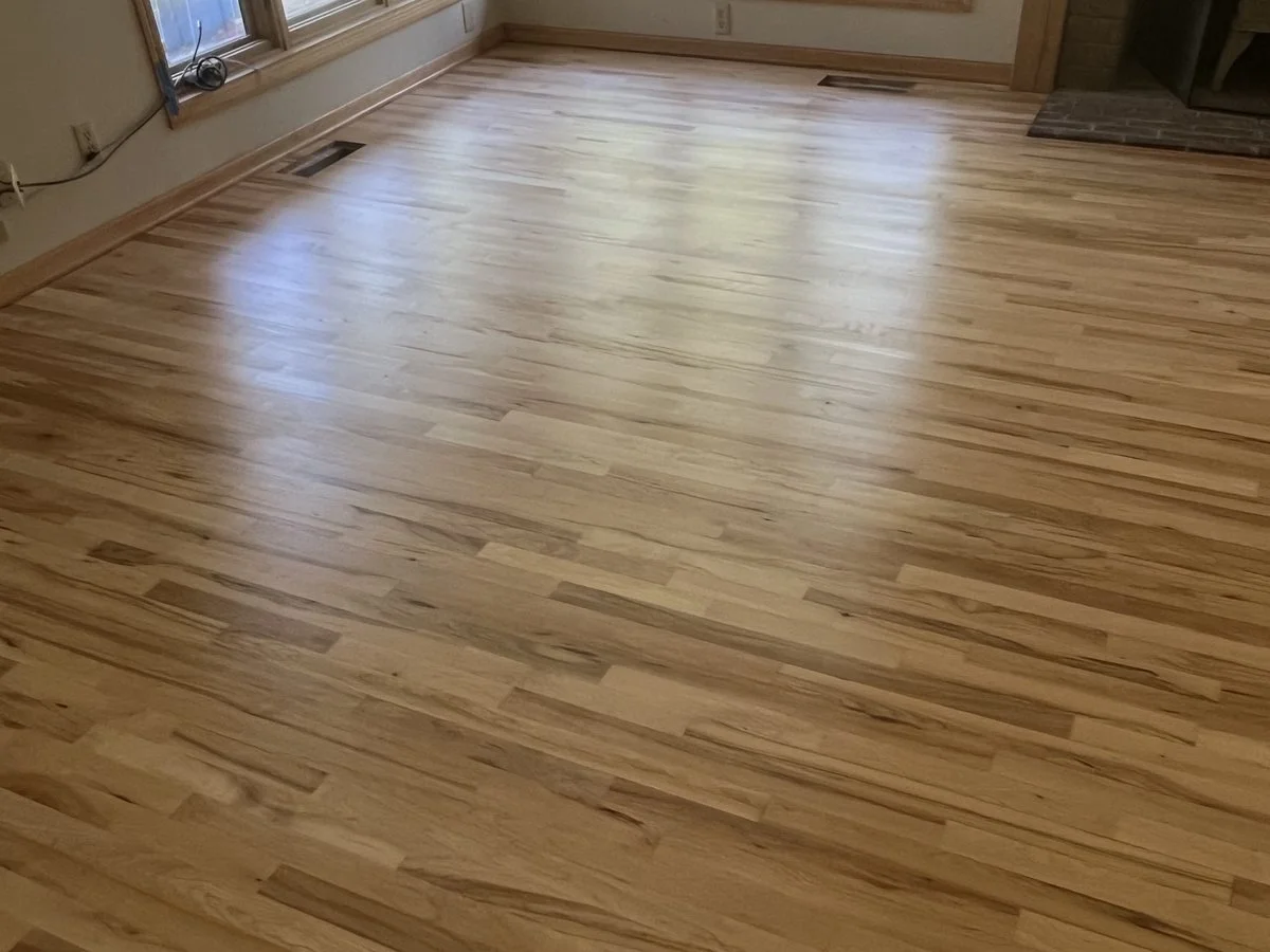Empty room with hardwood flooring, large window, and a brick fireplace in the corner.