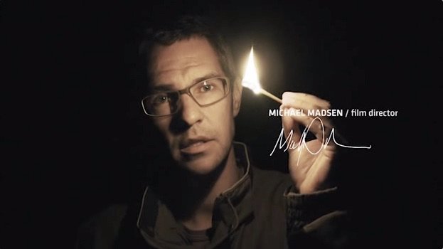 Michael Madsen, film director, holding a lit match in a dark setting