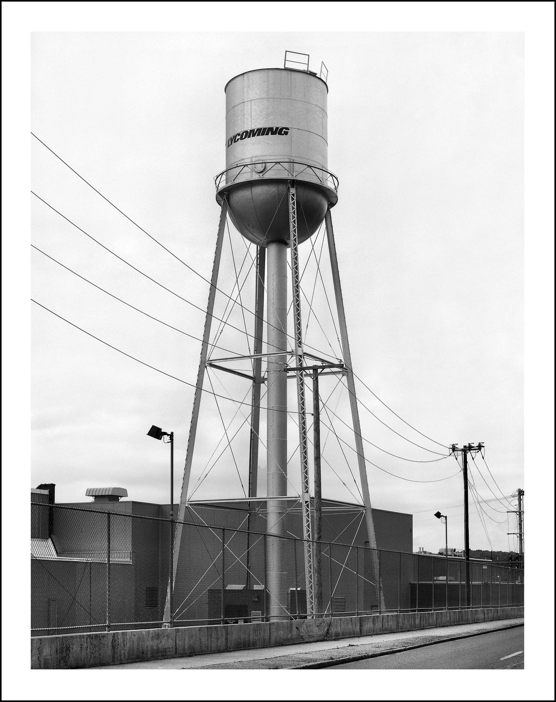 Black-and-white photo of a tall water tower labeled “Wyoming” above an industrial building and utility lines.