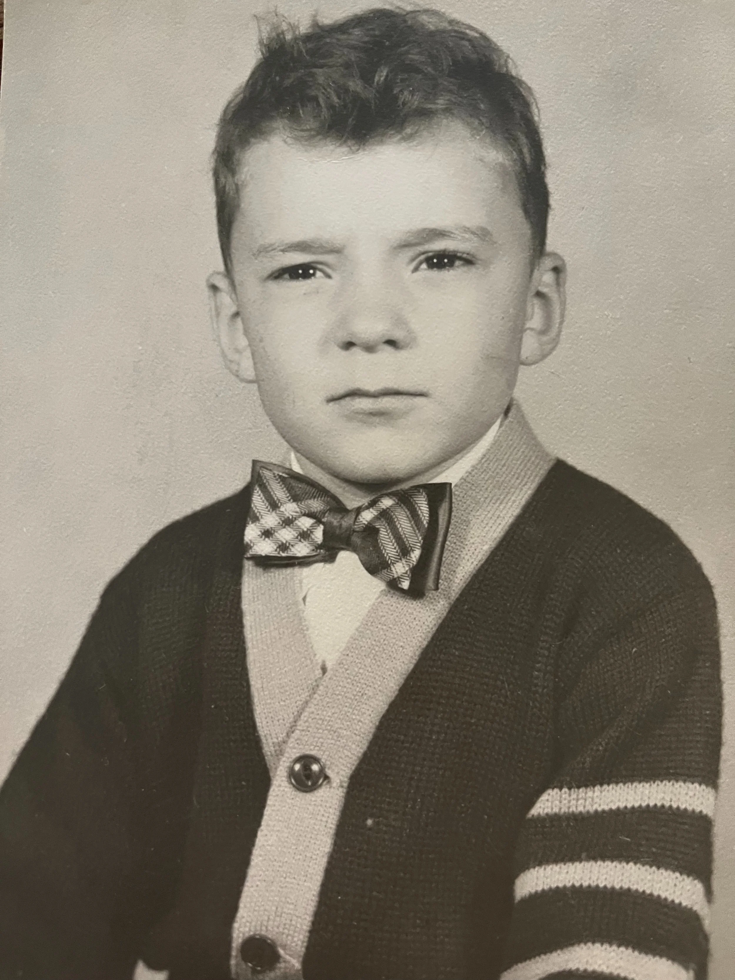 Vintage black-and-white portrait of a young boy wearing a bow tie, collared shirt, and suit jacket.
