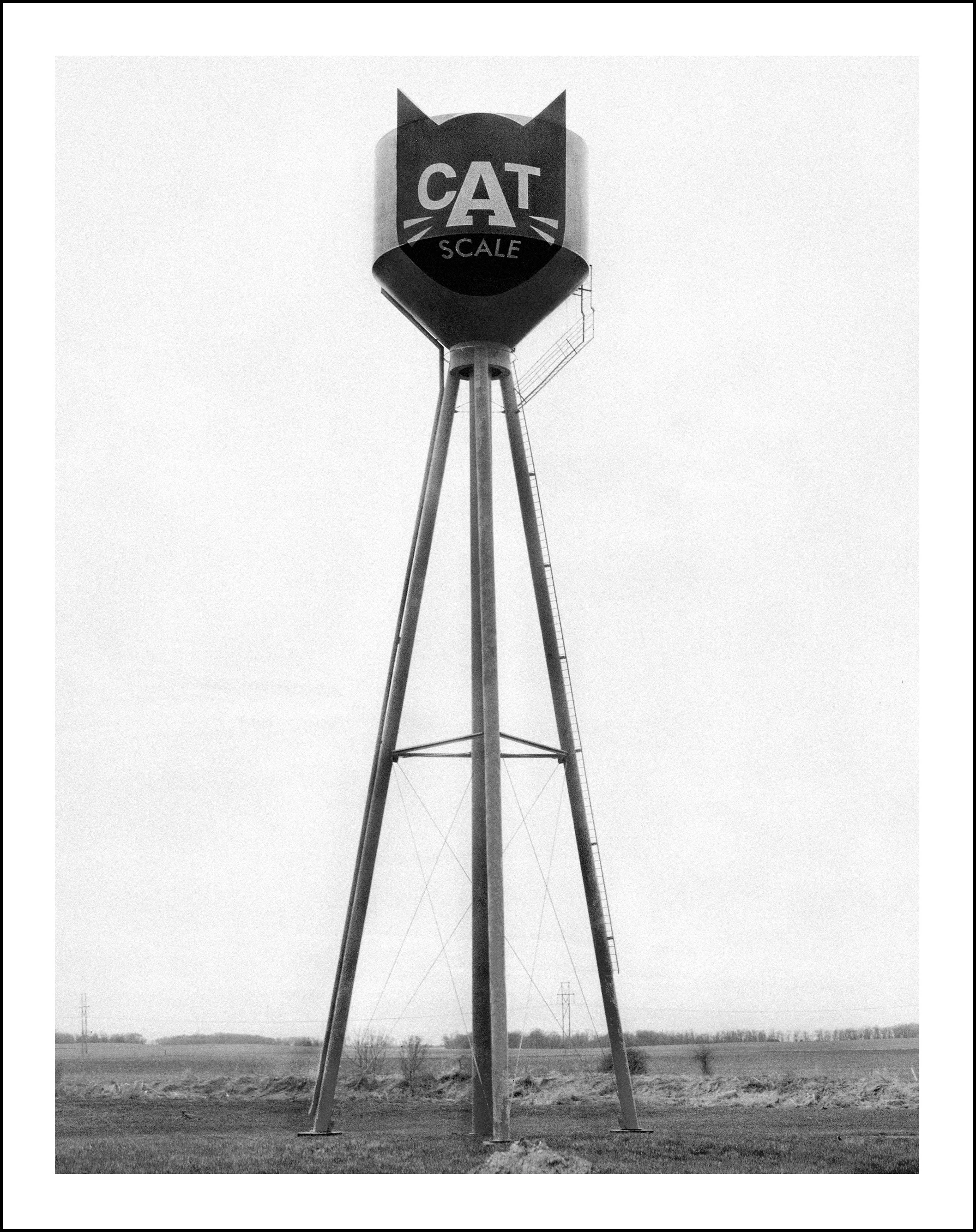 Black-and-white photo of a CAT Scale sign atop a tall industrial structure in an open field